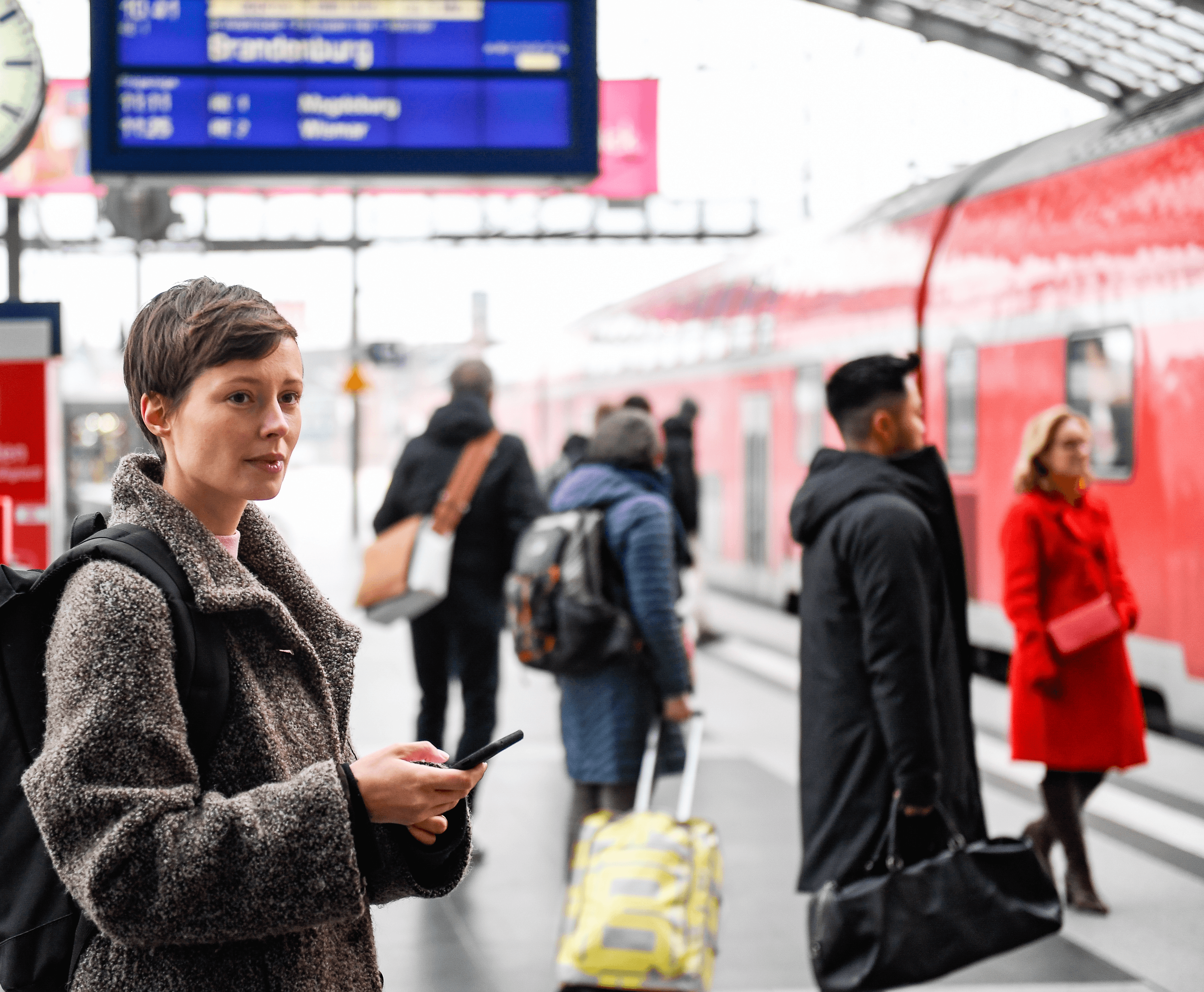 Eine Frau am Bahnsteig mit einem Smartphone in der Hand blickt auf einen einfahrenden Zug.