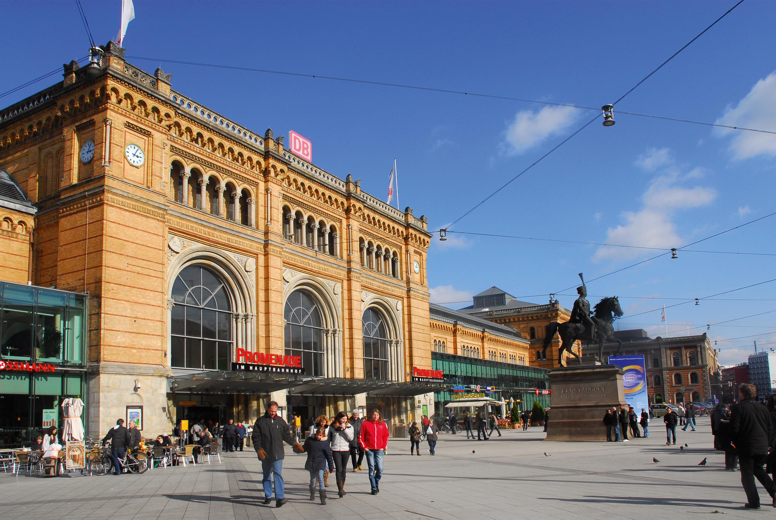 Menschen laufen, stehen oder sitzen auf Stühlen vor dem Empfangsgebäude am Hauptbahnhof in Hannover.