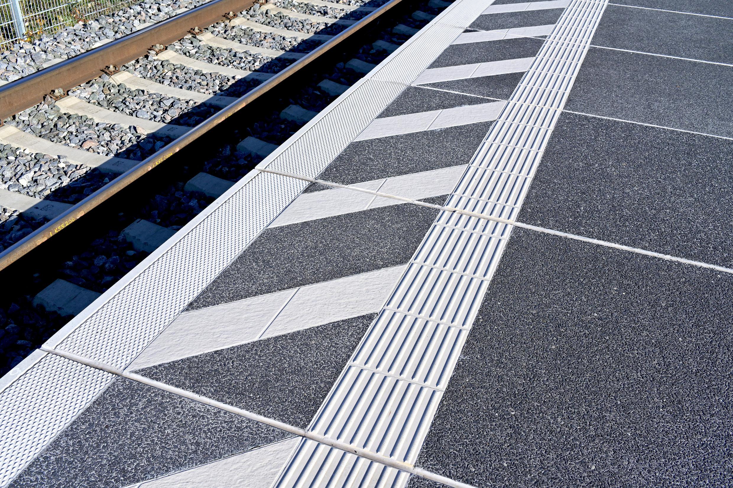Das Blindenleitsystem an einem Bahnsteig mit einem Gleis im Hintergrund.	
