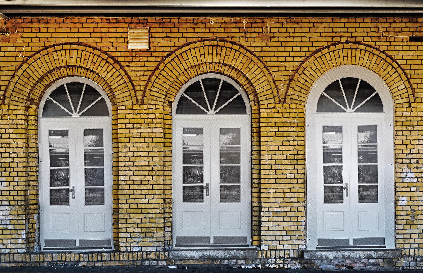 Drei bodenlange Fenster eines Gebäudes nebeneinander.