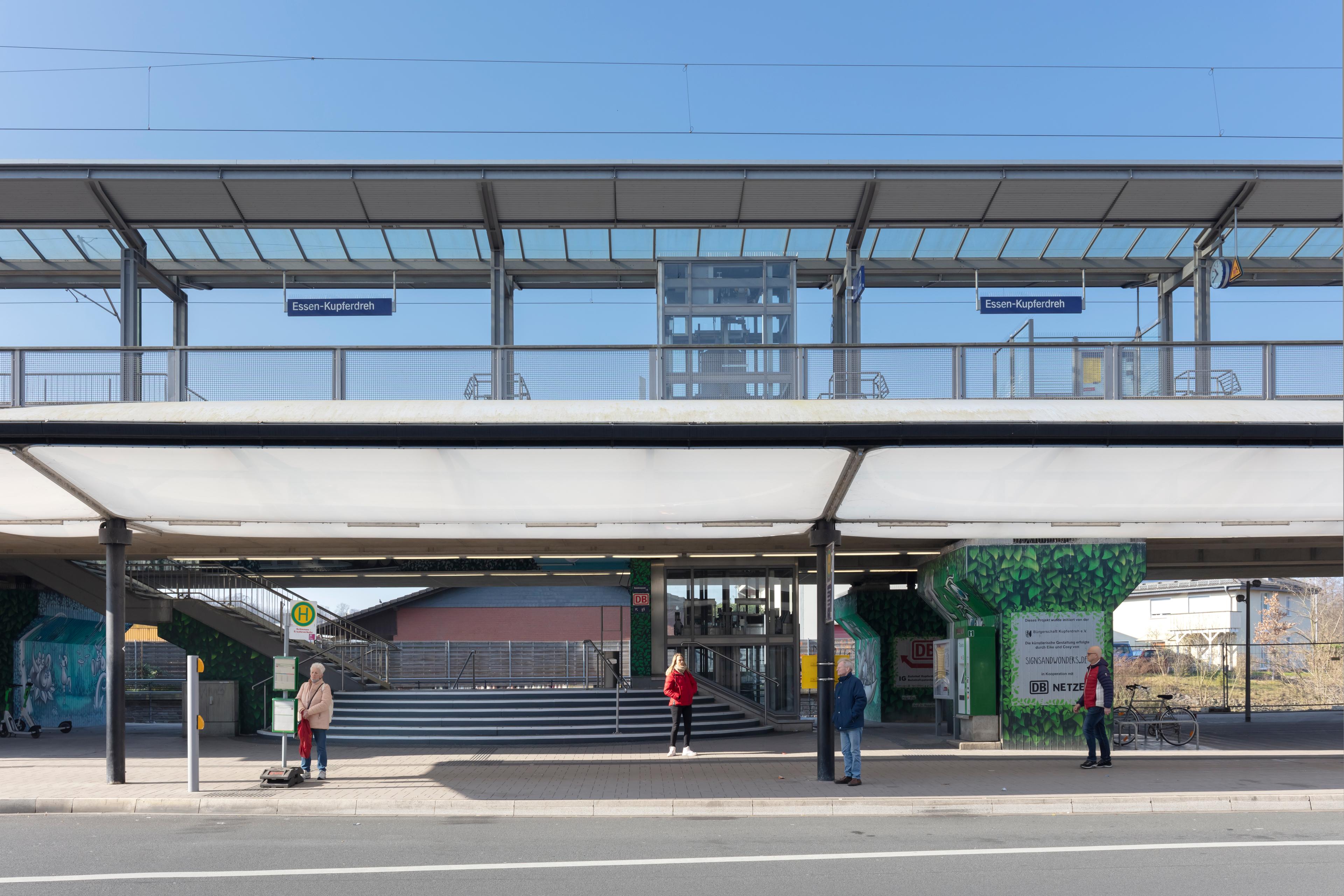 Reisende warten an Bushaltestelle vor dem Bahnhof.