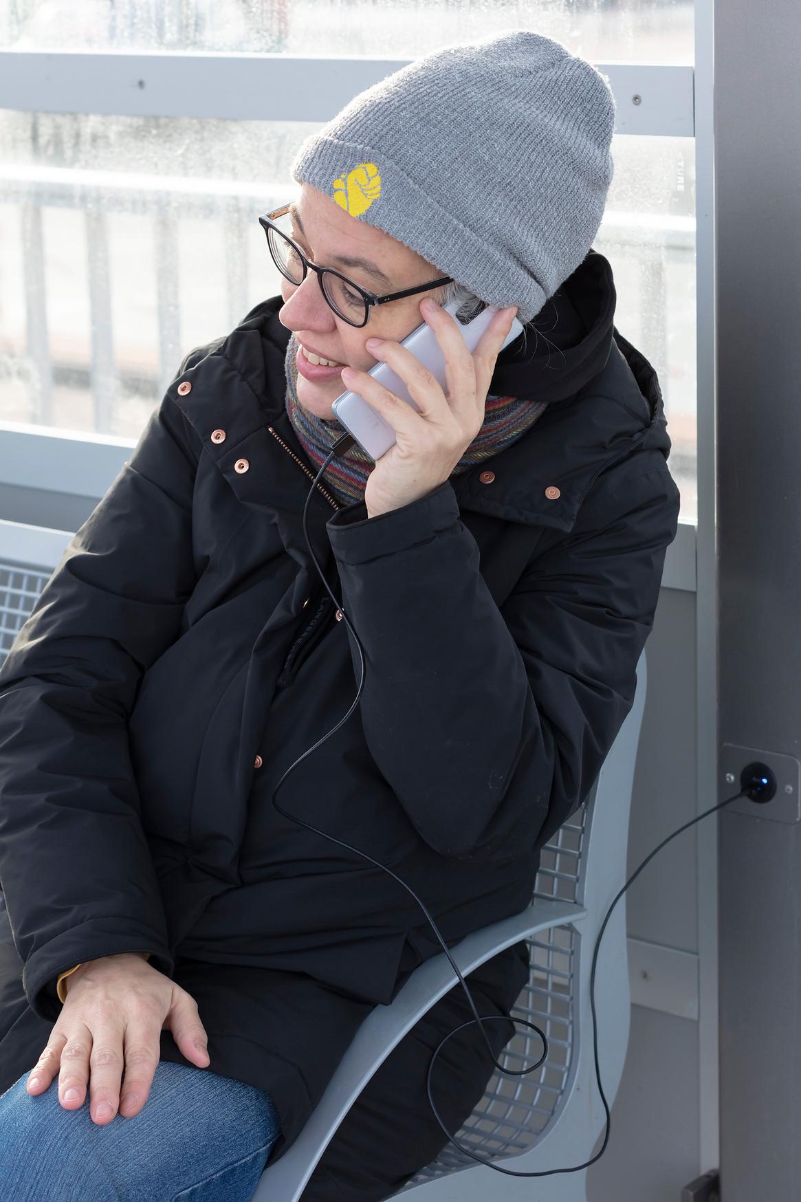 Eine Person telefoniert, während ihr Smartphone am Wetterschutzhäuschen läd.