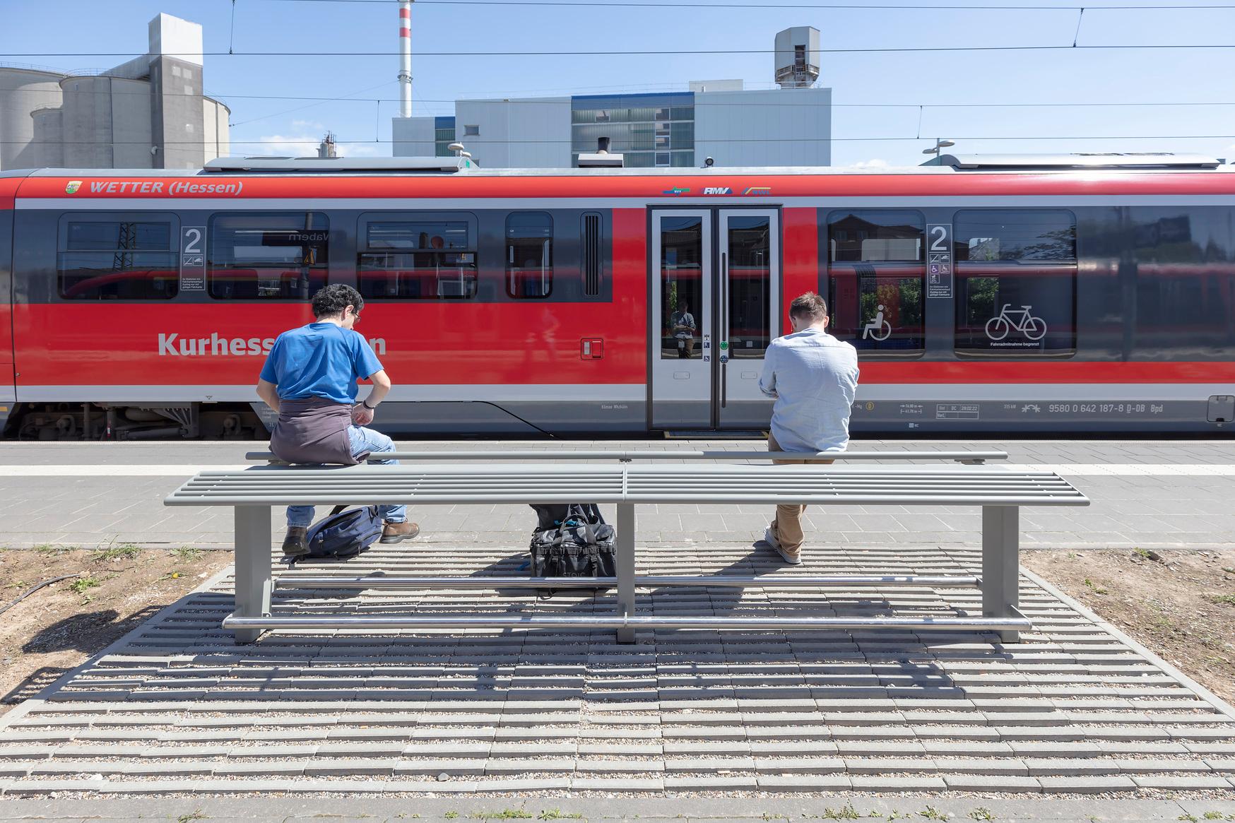 Zwei Personen sitzen auf neuen Sitzmöbeln am Bahnsteig.