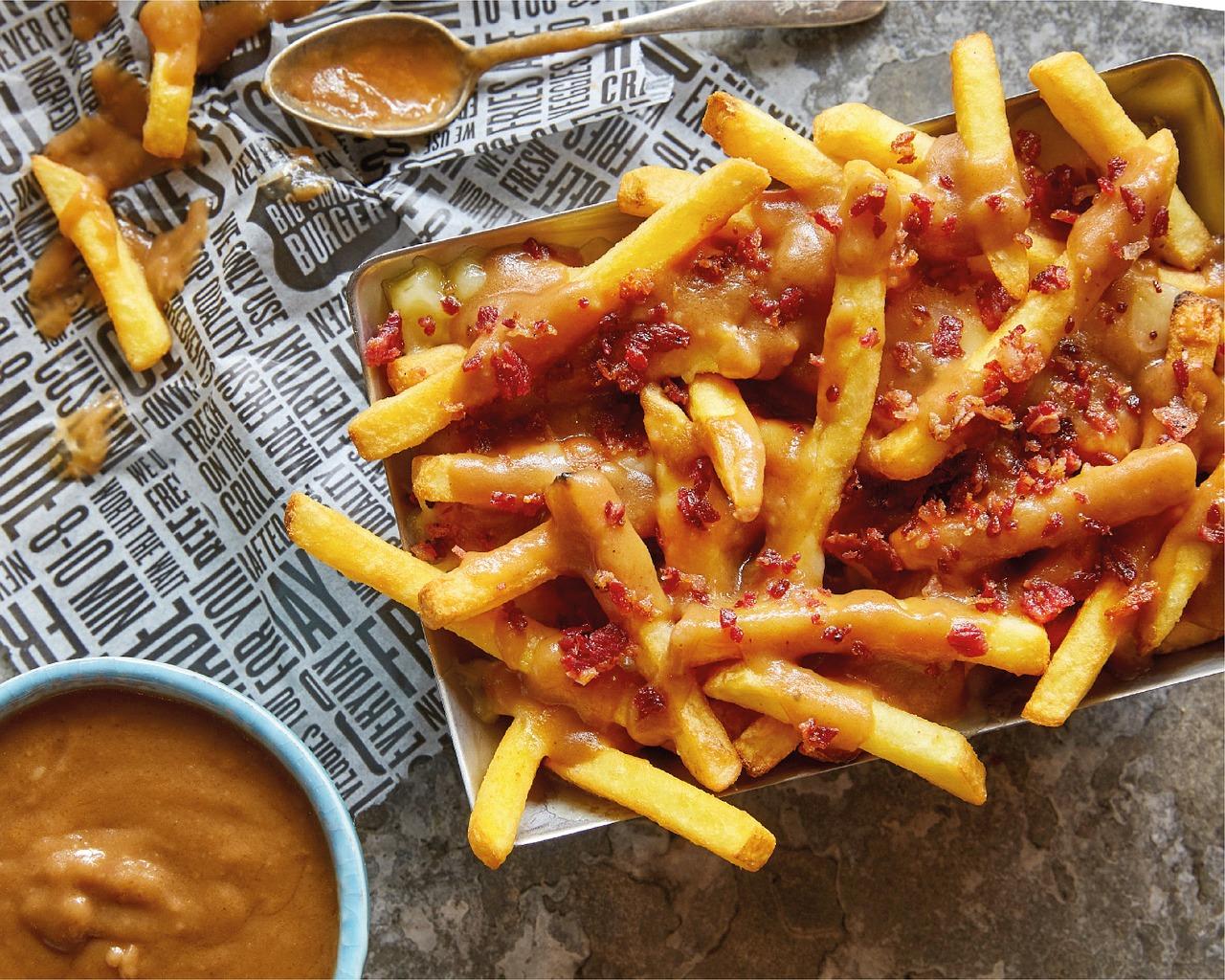 Goldgelbe Pommes frites garniert mit einer cremigen Sauce und knusprigen Bacon-Würfeln.