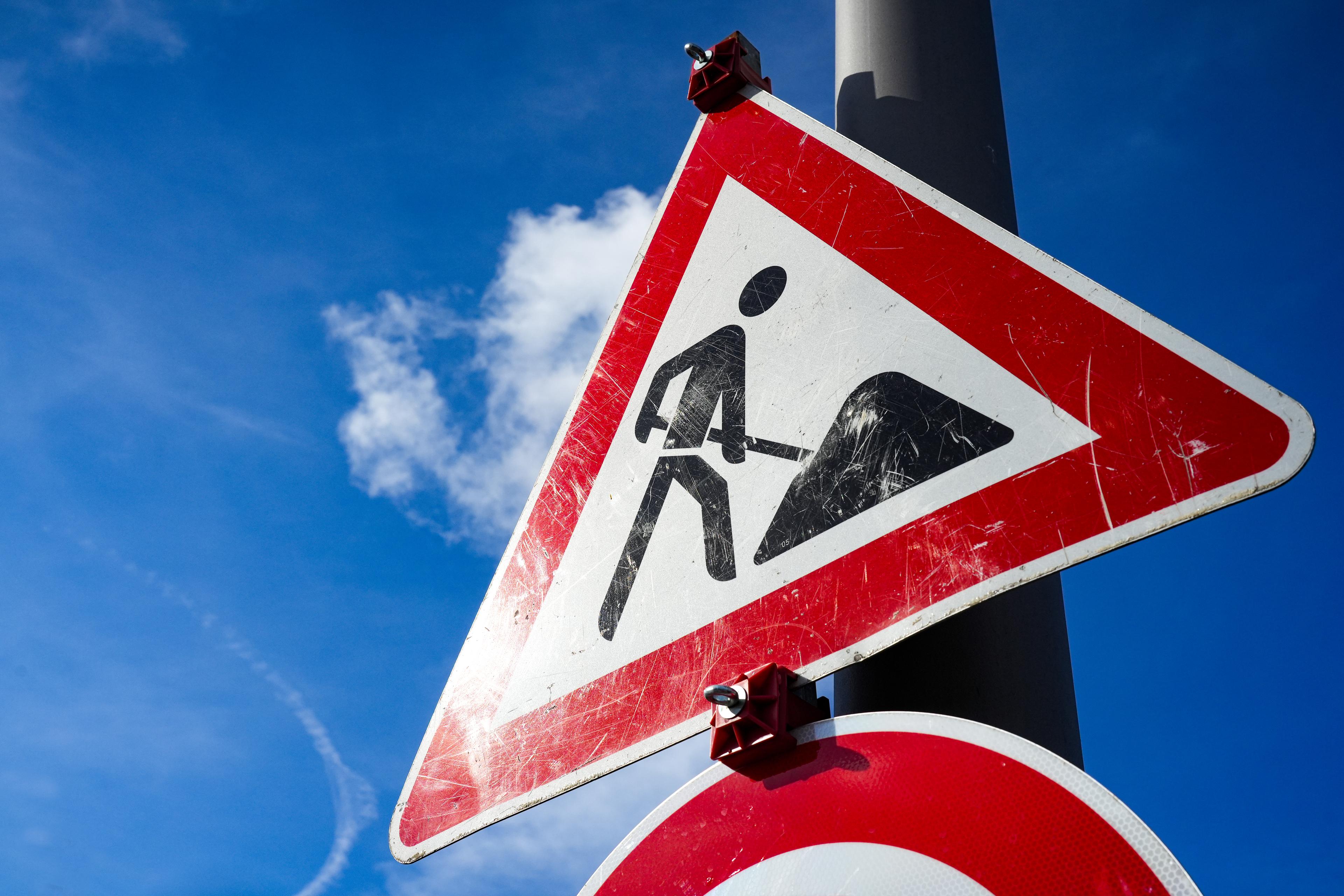 Dreieckiges Verkehrsschild "Achtung Baustelle" mit roter Umrandung. 